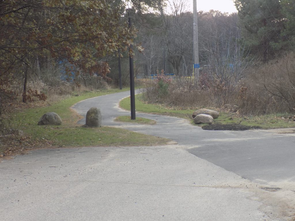 multi use path entry entrance with decorative boulders and lighting heading into the woods.