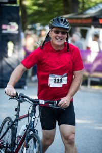 A man with red t-shirt and black helmet is standing next to his bike 