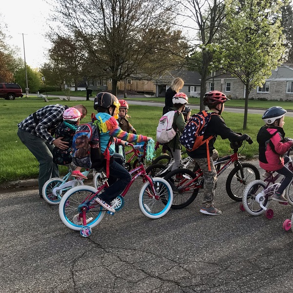 A group of student bicyclist at a Bike to School Event with parents walking along side encouraging them.