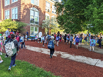 Bunch of children walking up to a large brick school.