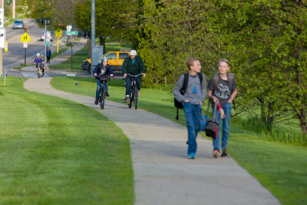 View of treelined sidewalk with two cyclists in the background and two student walkers in the foreground.