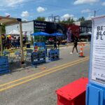 A brightly painted parklet is set up in a closed road area as part of the Better Block Flint event. Poster for the event seen in the foreground.