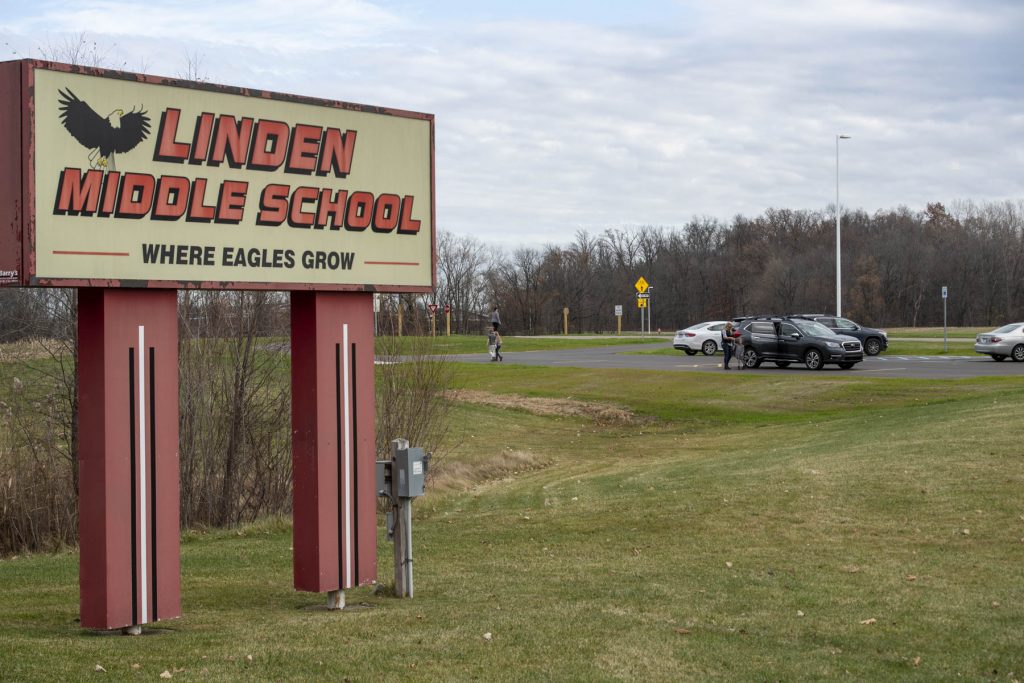 Linden Middle School sign with Eagle mascot and their motto "where Eagles grow" is in the foreground with parking lot and signs from the the rectangular rapid flashing beacon crossing in the background
