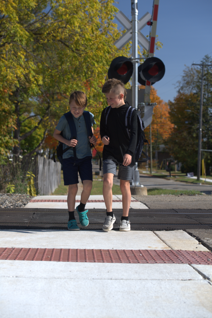 Two smiling children cross railroad with the new rubber flangeway and concrete ADA approaches.