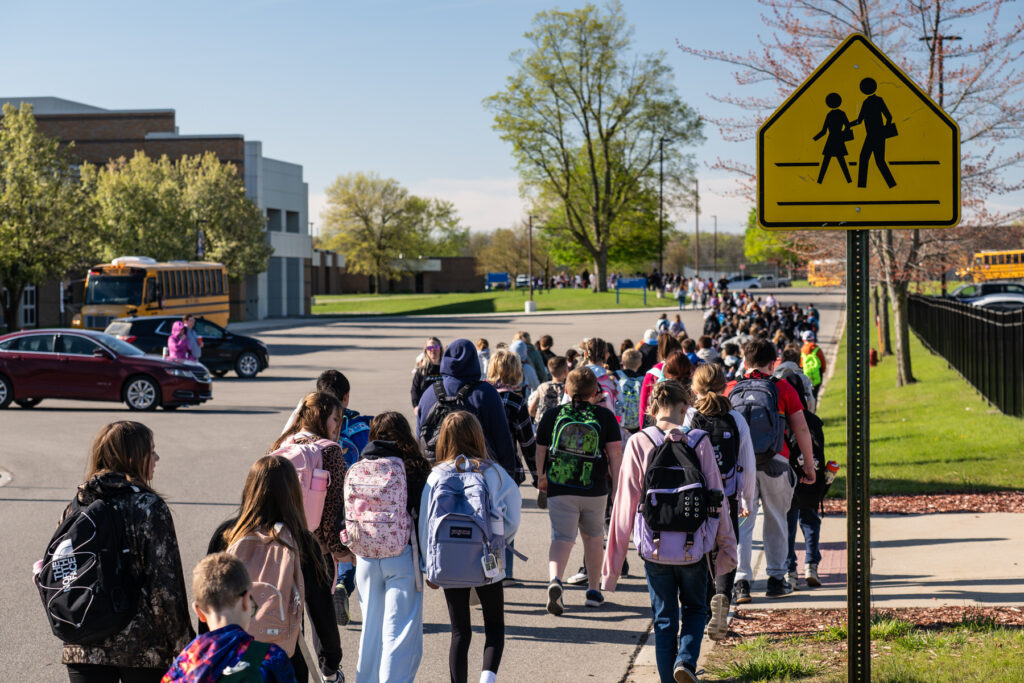 Imlay City students walk from a remote drop site to school with school crossing sign in the foreground.