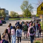 Imlay City students walk from a remote drop site to school with school crossing sign in the foreground.
