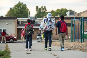 Three Windemere Charter Academy students in the foreground walk across playground sidewalk towards their school building in Lansing.