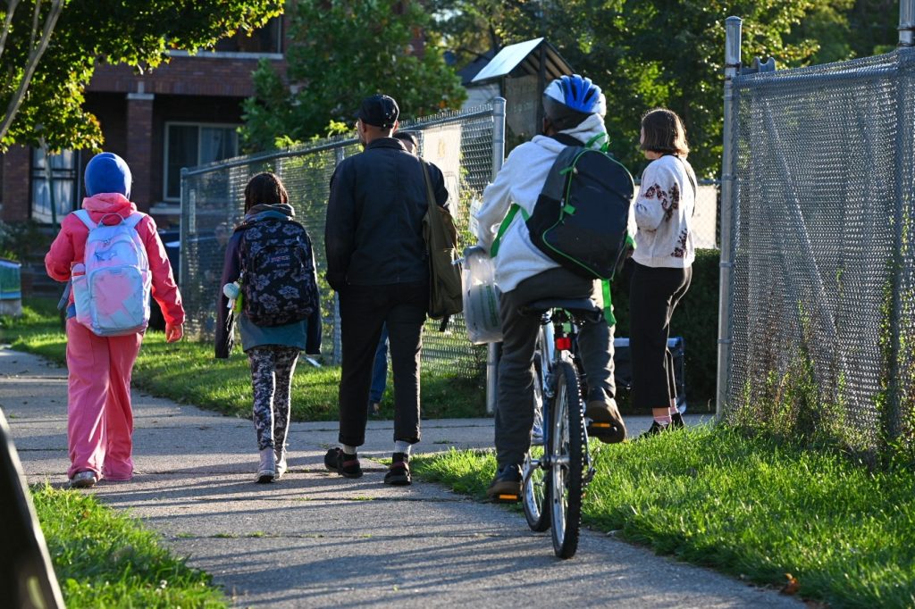 Students walk and bike along a sidewalk to the school entrance.