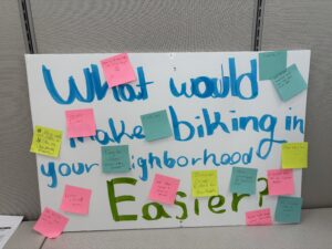 Posterboard with the question asking "What would make biking in your neighborhood easier?"that is covered in post-it notes with responses. 
