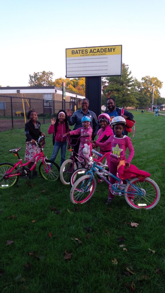 girl student bicyclists group around SRTS coordinator and their school sign.