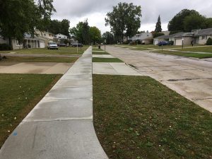 Residential area with view down new concrete sidewalk running along a street.