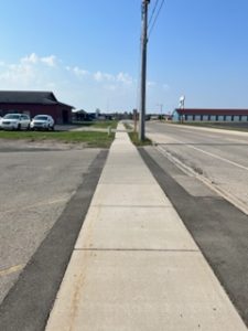 Sidewalk running across the middle of image with asphalt on each side which creates contract and visibility of the pedestrian space.