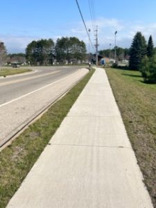 Sidewalk extending alongside roadway with both curving to the left in the background