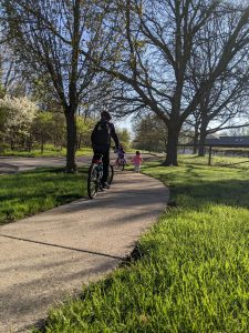 Two students from Islamic School of Grand Rapids bike along on sidewalk with small child running behind