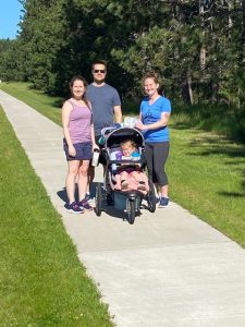 Three adults with a child in a stroller stand within the sidewalk