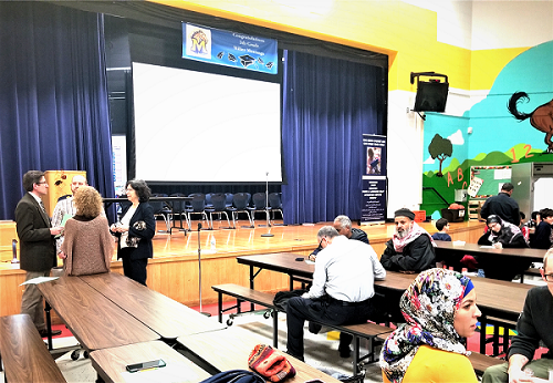 action planning meeting in school auditorium with stakeholders seating at cafeteria tables before a presentation screen