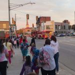 Students and parents walk in a scattered group near a lighted intersection in Grand Rapids with firefighter escort as part of the Sibley Elementary 2023 WR2SD event.
