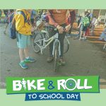 Adult mechanic helping fix a student's bike brake cables with Bike & Roll to School Day logo at the bottom of the image