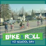 Bike train of students bike in line behind adult supervisor down roadway as part of Grayling Bike and Roll to School Day event. Bike and Roll to School Day logo