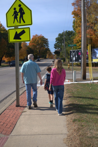 Two adults walk and one child approach a street crossing, new sidewalk can be seen at the intersection. Photo Credit MDOT
