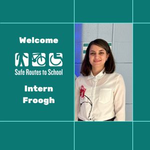 Square graphic with teal background and light teal grid lines around an images of a woman with shoulder length brown hair in a white-button-up- collared shirt with a pink flower on it. Text on the left reads "Welcome (Safe Routes to School logo) Intern Froogh"