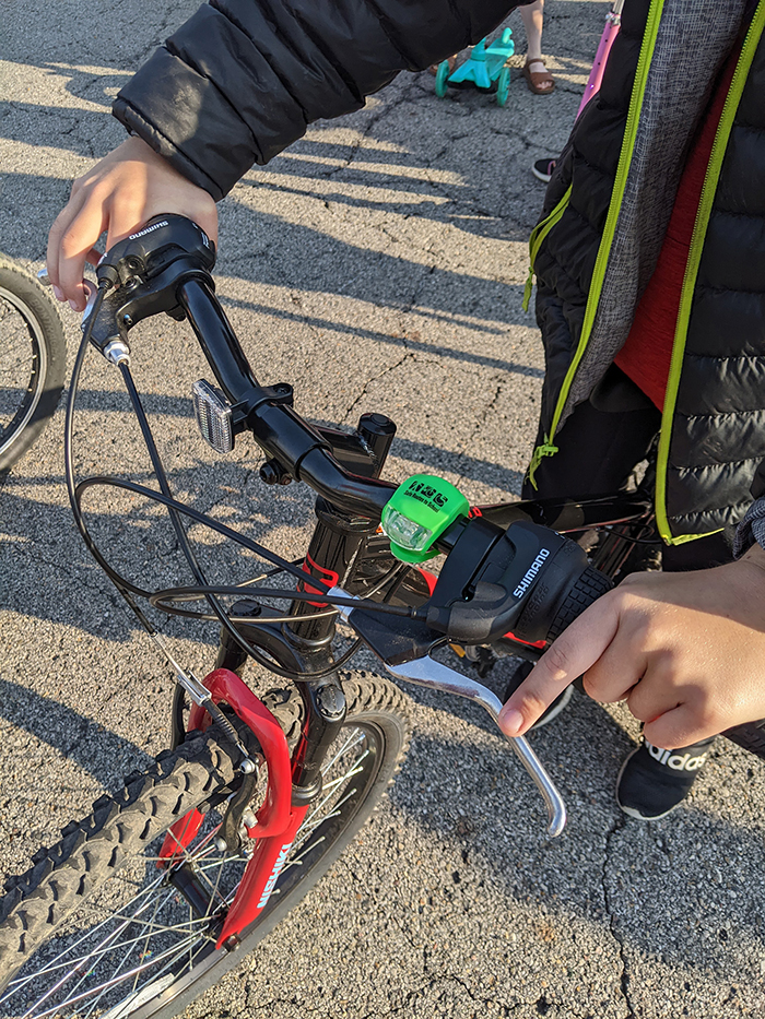 Close up of the handle bar of a child's bike with SRTS green light attached to it.