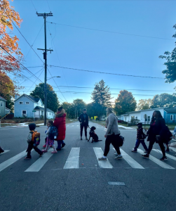 Several children and adults cross a street using striped crosswalk with a support dog from Charlotte’s Social and Emotional Learning program.