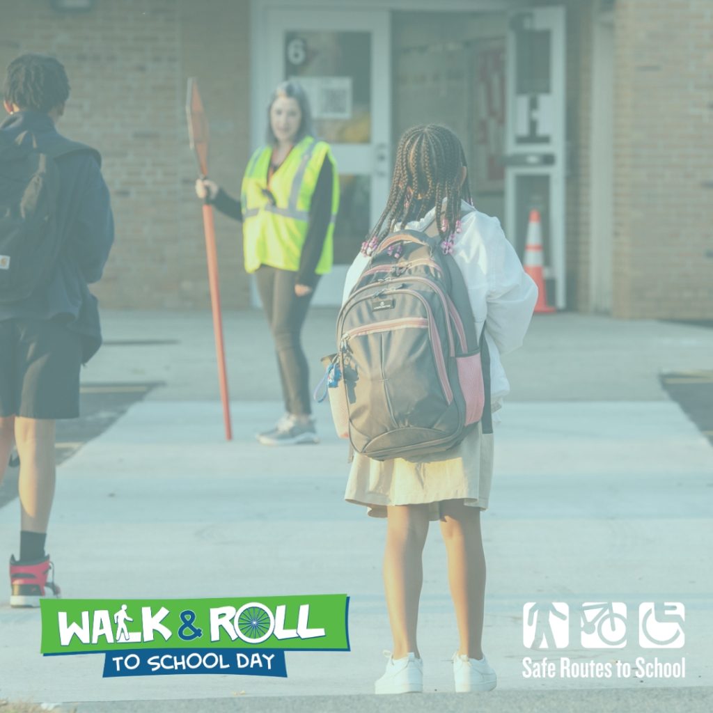 Black Girl with braids and a black and pink backpack waits in the foreground at crossing to the school which has a white, woman, crossing guard in the crossing holding a stop sign. Another student is crossing on the left side of the image.